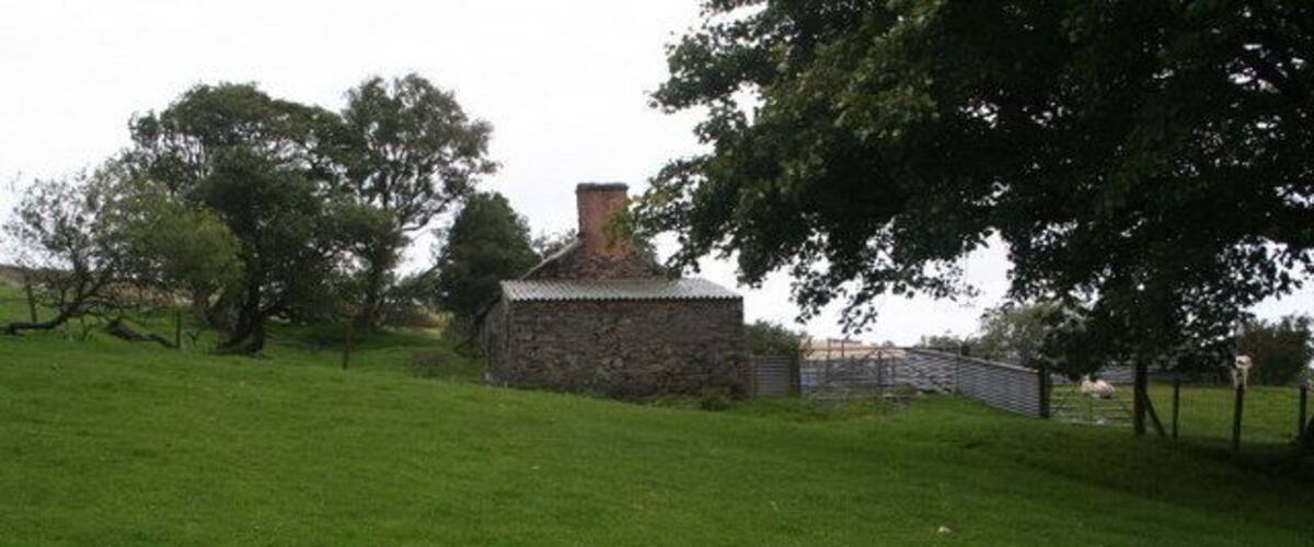 A stone building with a chimney, surrounded by a grassy field and trees.