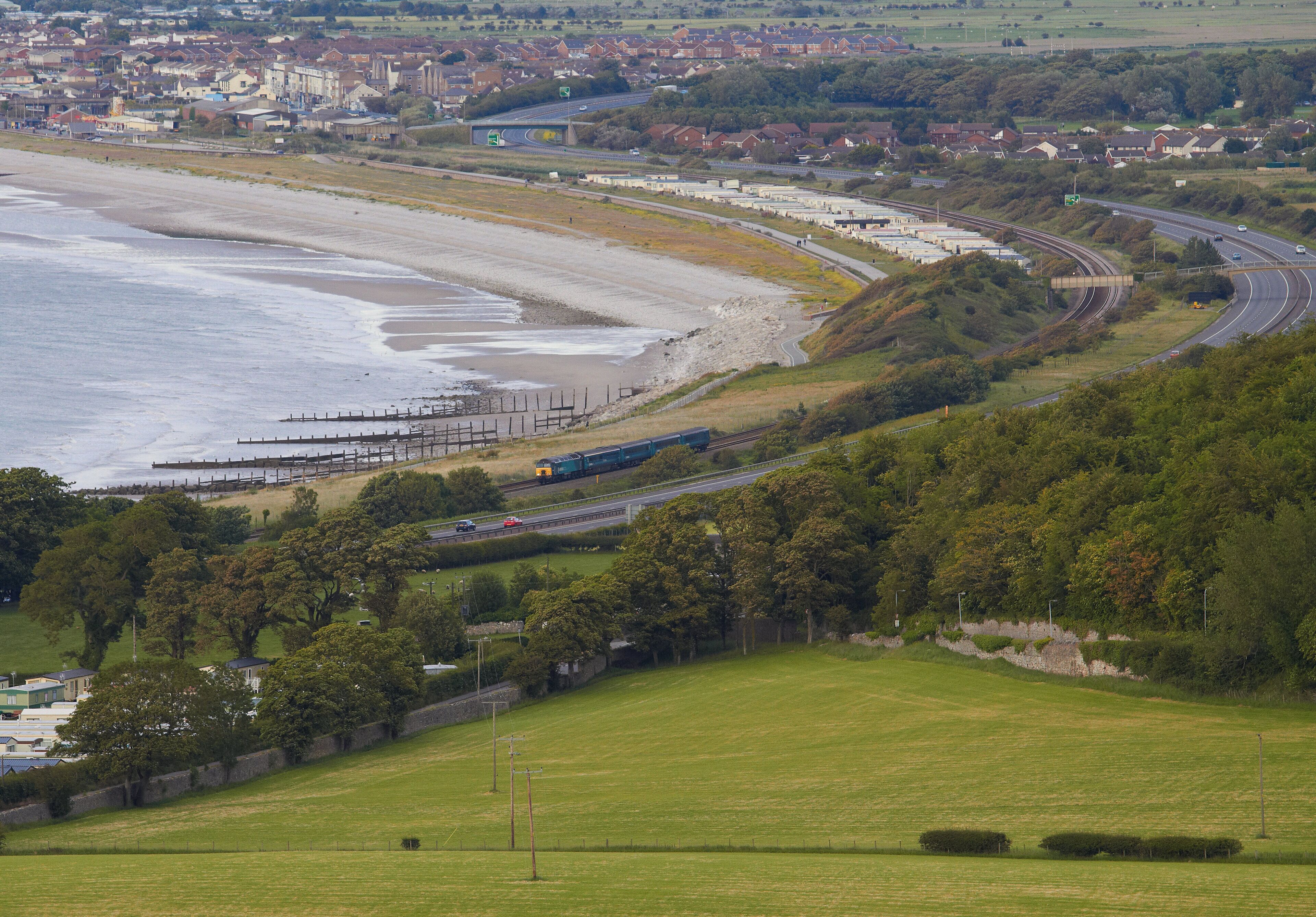 A coastal town with a beach, railway tracks, and a highway curving through the landscape.