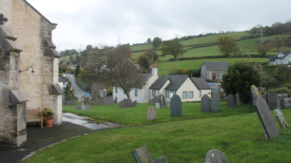 A cemetery with headstones, a stone building, and a grassy area.