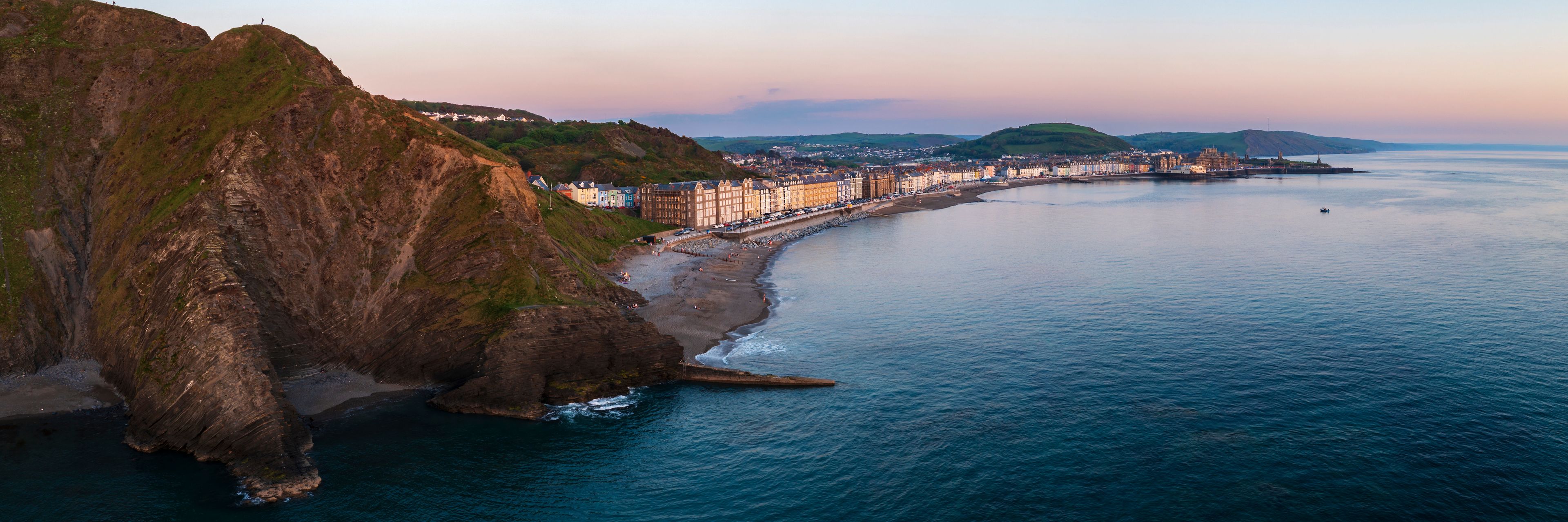 A coastal town with a long promenade, cliffs, and a calm sea.