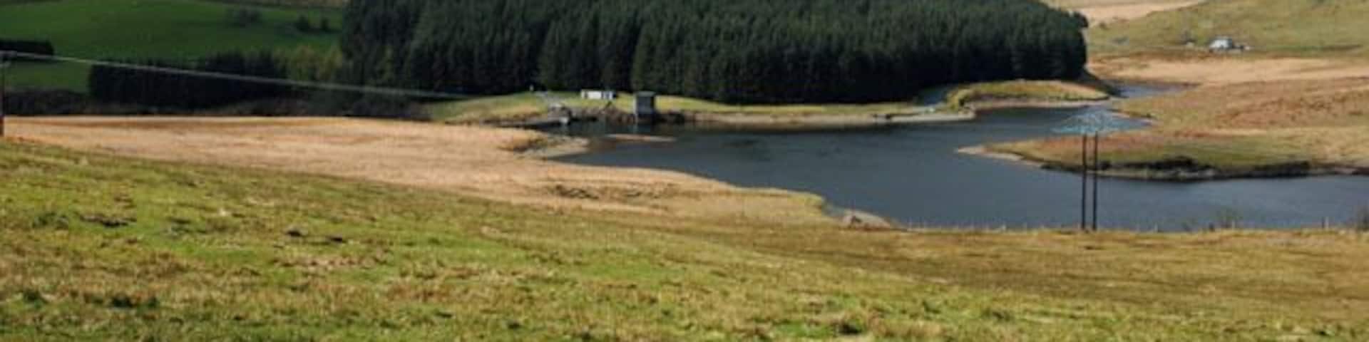 A lake surrounded by forested hills and open fields.