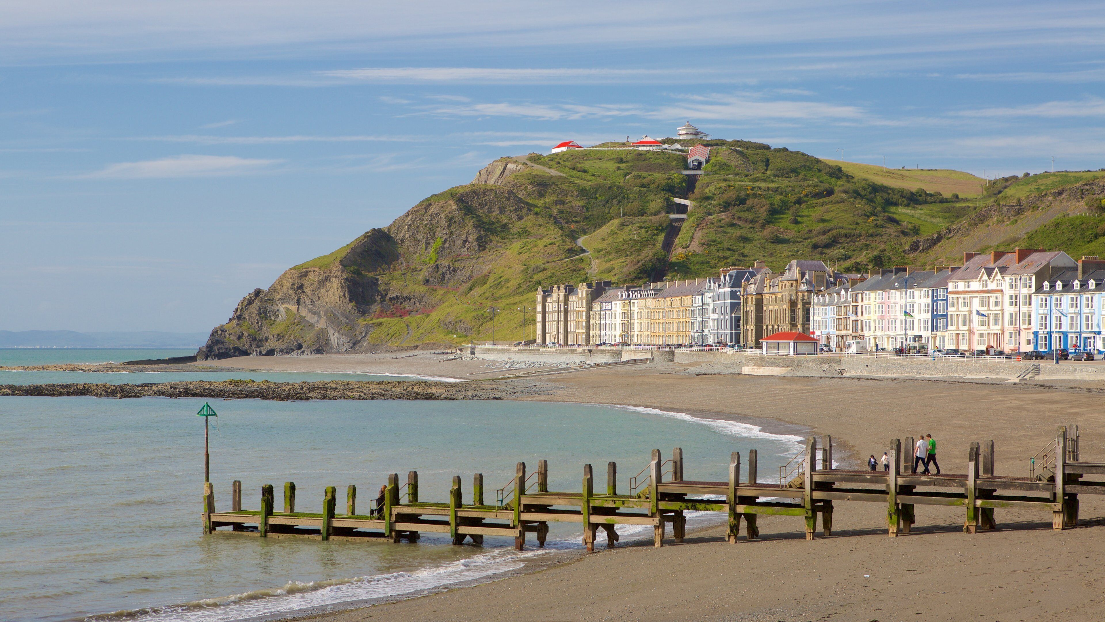 A coastal town with colorful buildings, a lighthouse on a hill, and a wooden pier.