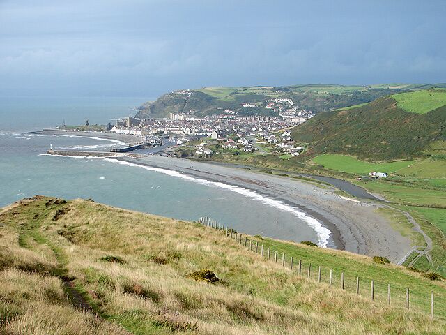 A coastal town with a beach, a lighthouse, and rolling hills.