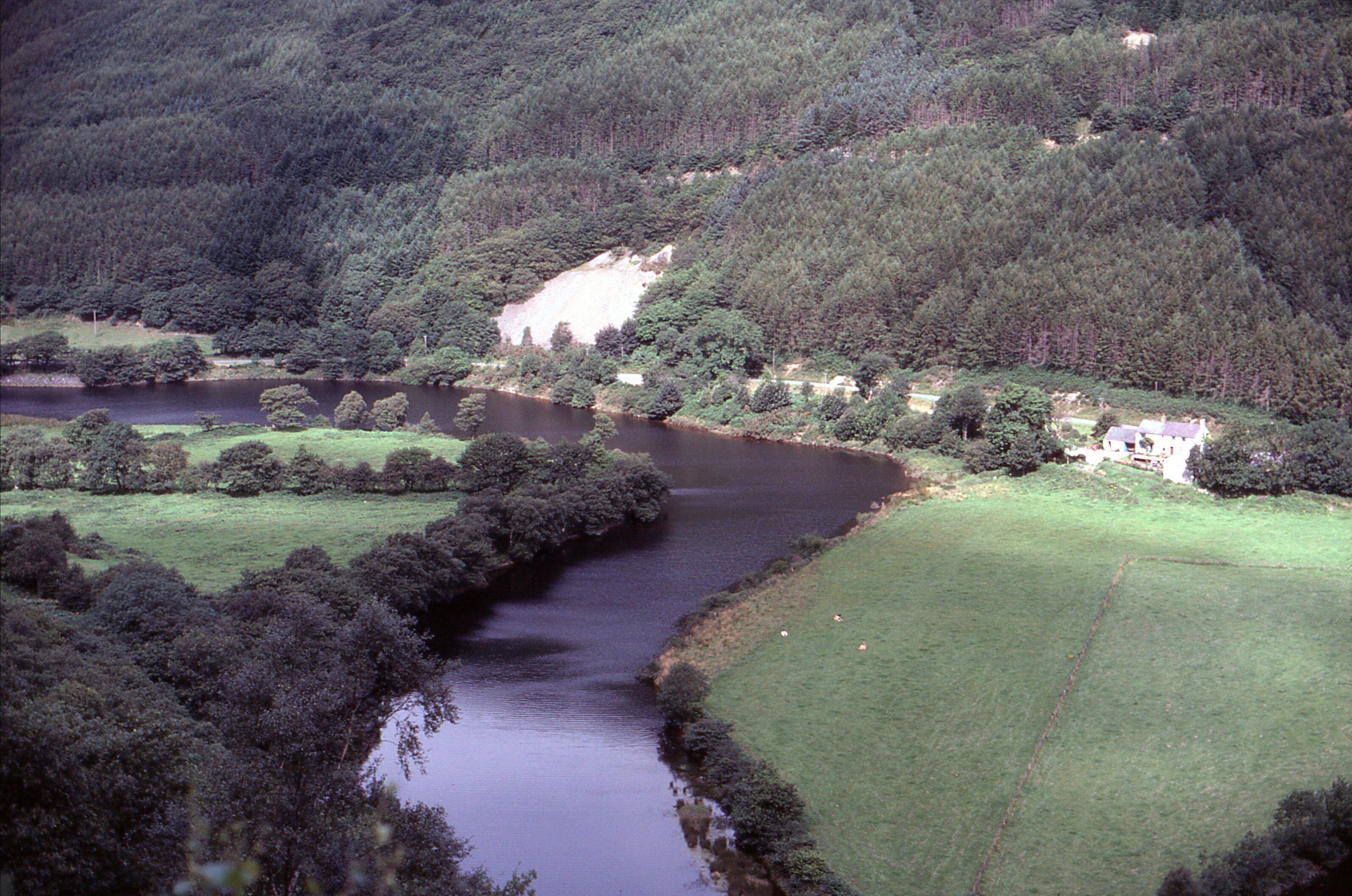 A river winding through a forested valley with a house on a hill.