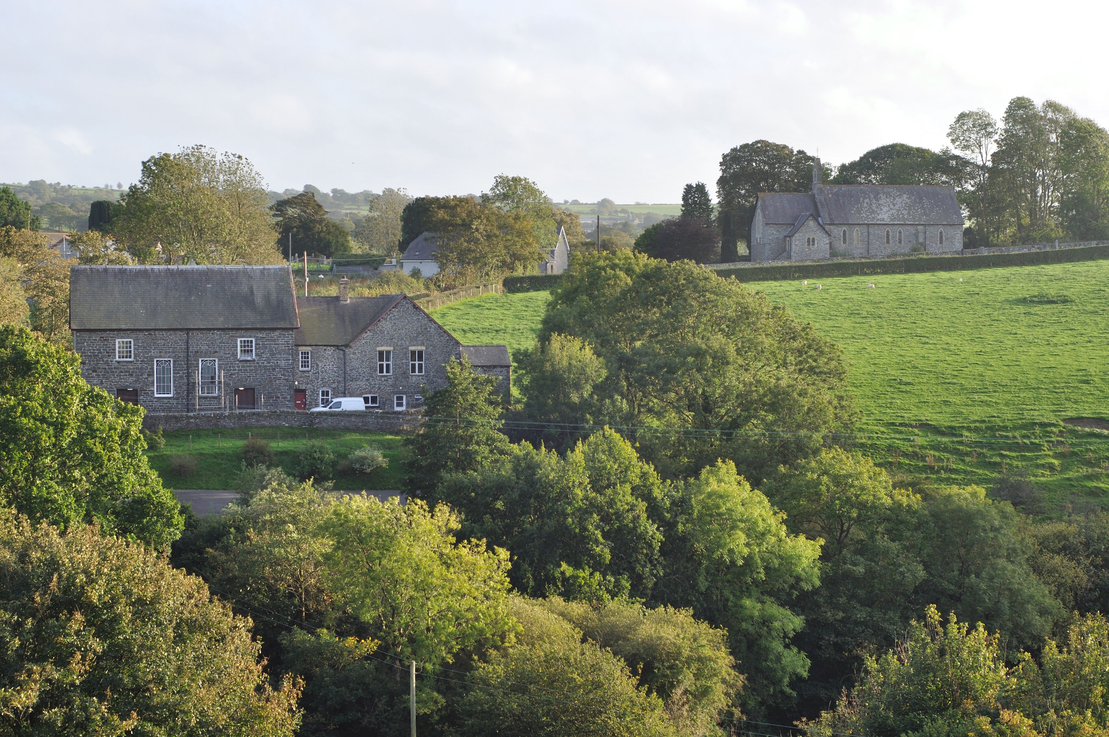 A rural landscape with stone houses, a green field, and trees.