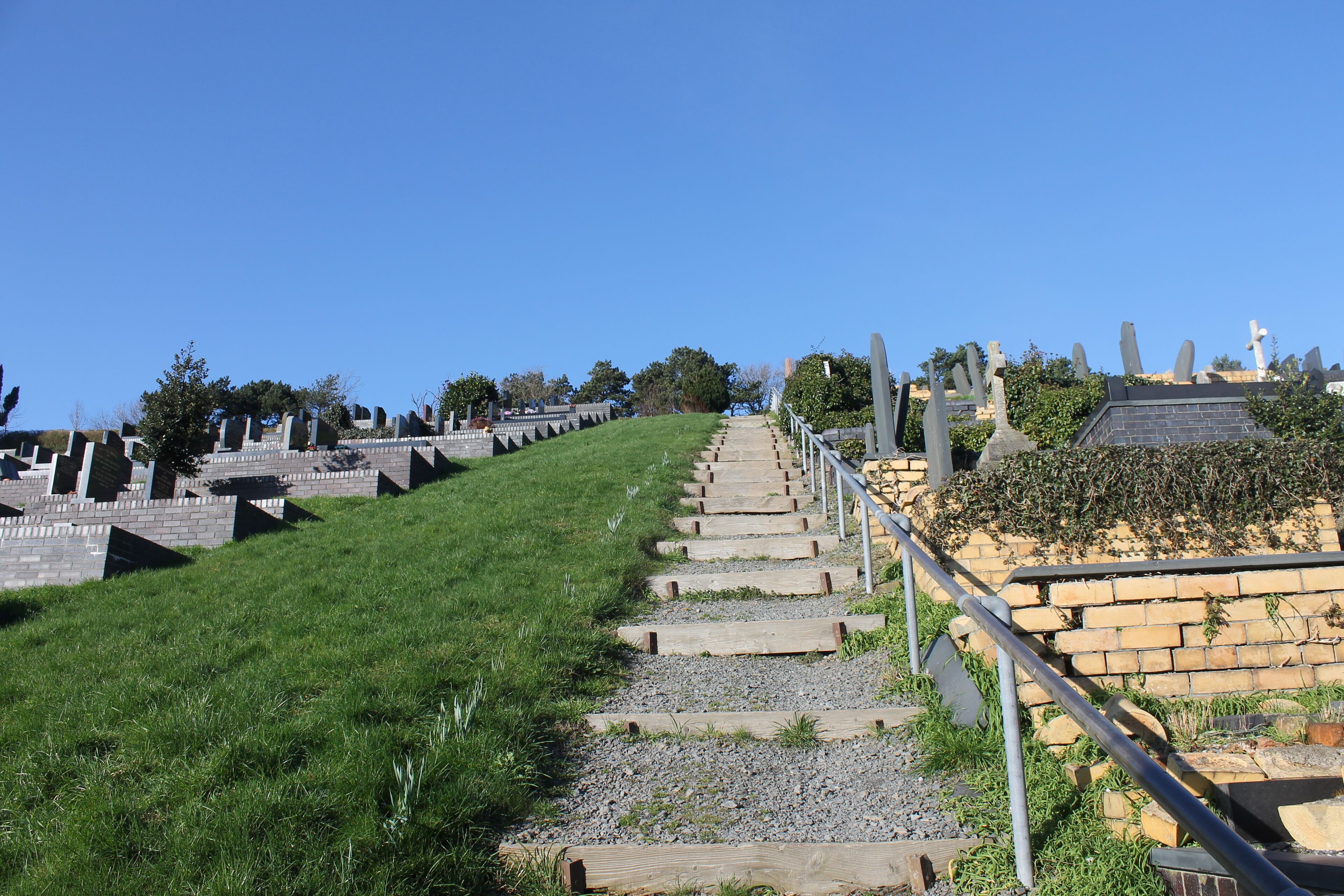 A pathway leading up a hill with stone markers and a brick wall on the right.