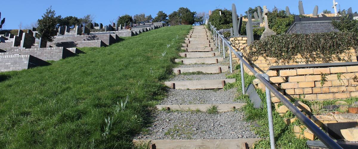 A pathway leading up a hill with stone markers and a brick wall on the right.