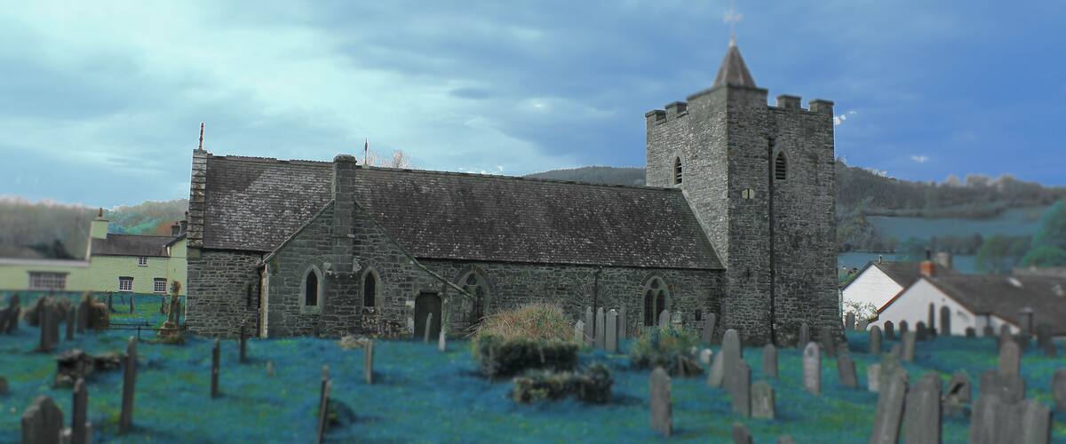 A stone church with a bell tower and a graveyard in the foreground.