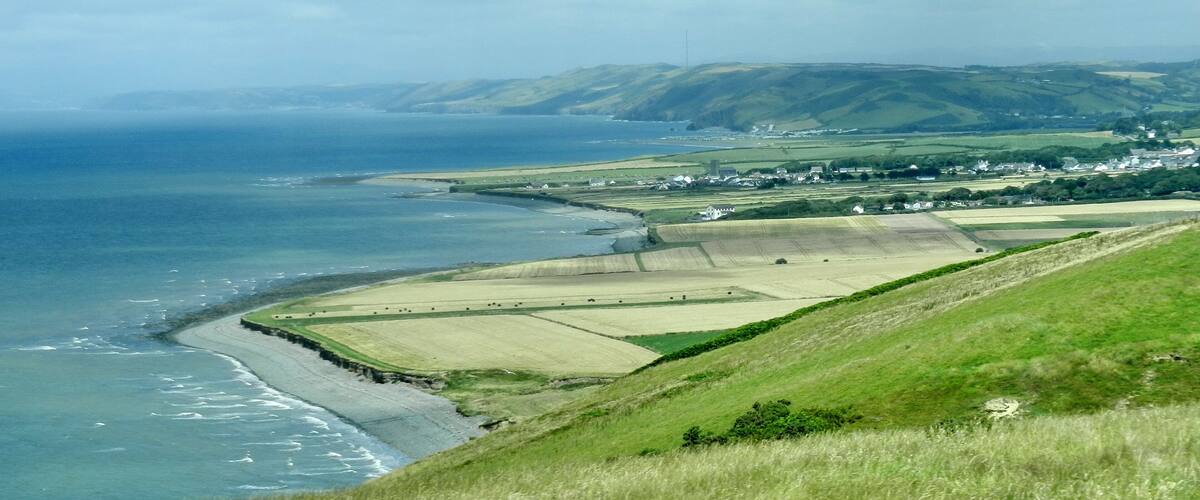 A coastal landscape with fields, a beach, and a village in the distance.