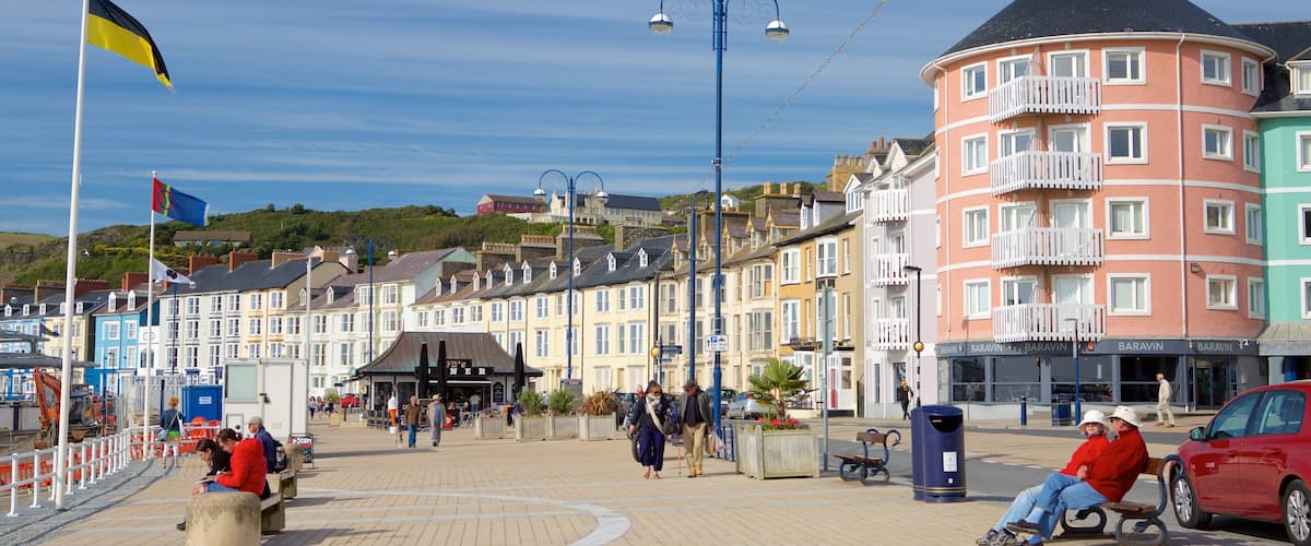 A coastal promenade with colorful buildings, a flag, and people walking.
