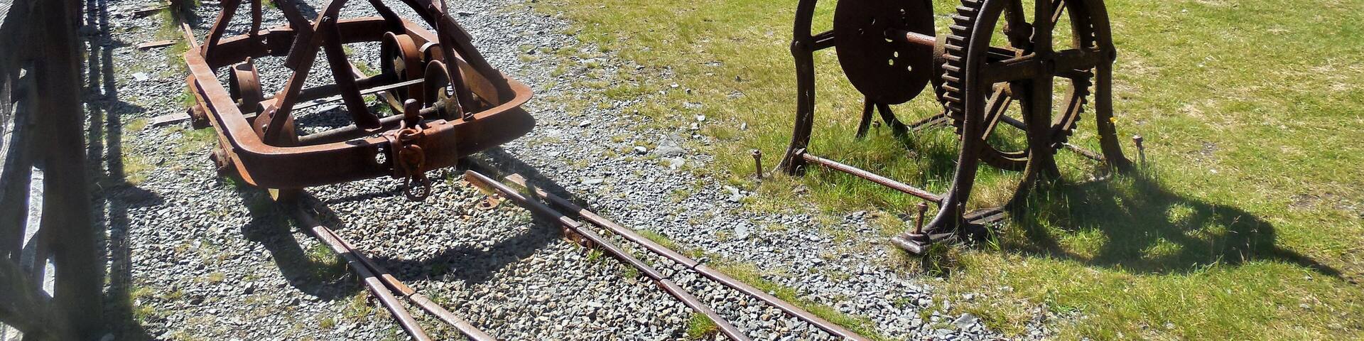 A historical site with old railway equipment, stone buildings, picnic tables, and a sign for the 'Trail'.