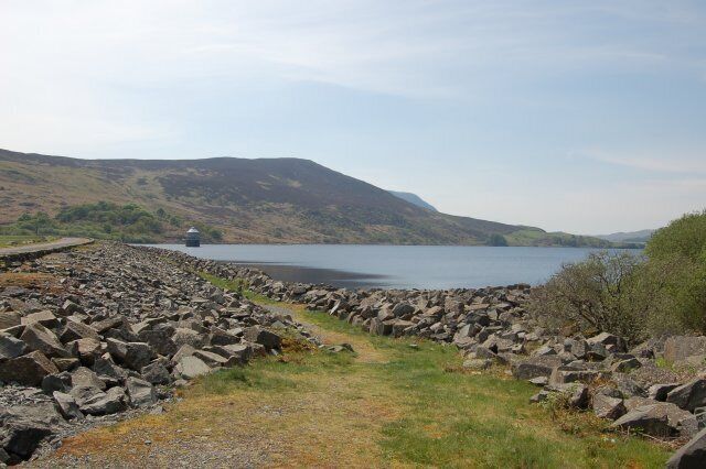 A rocky shoreline with a body of water, hills in the background, and a small structure on the water.