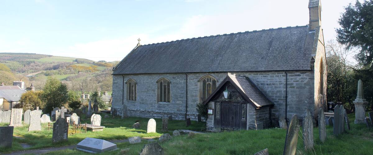 A stone church with a steeply pitched roof and a small bell tower, surrounded by a cemetery with headstones.