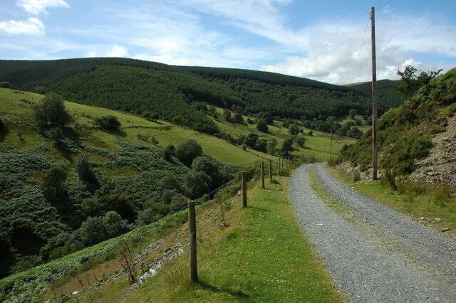 A gravel road winding through a green valley with hills in the background.