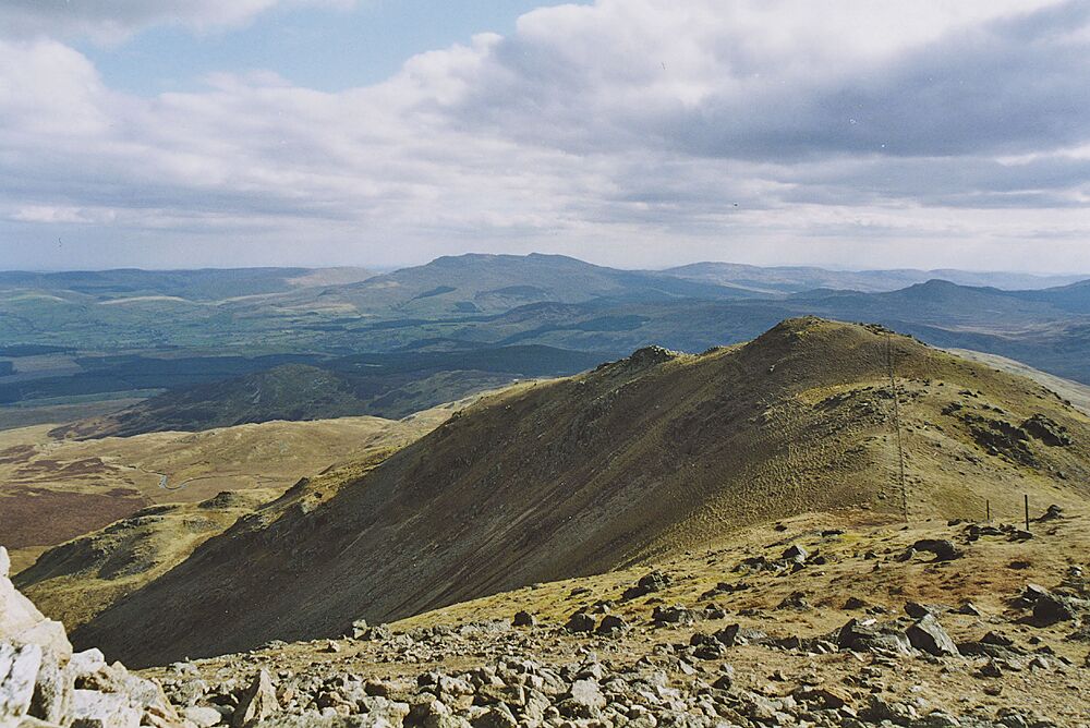 A rugged mountain landscape with rocky terrain and distant hills under a partly cloudy sky.