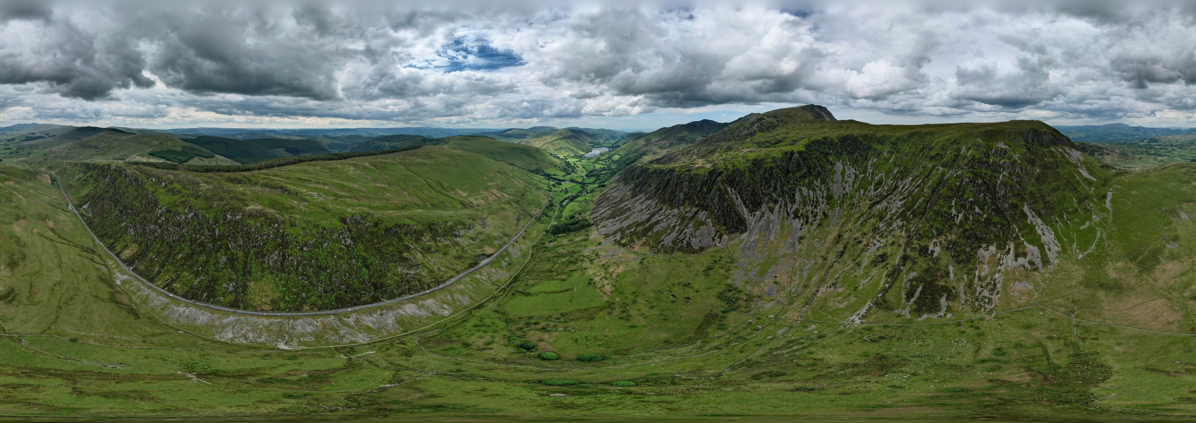 A winding road through a mountainous landscape with green hills and a cloudy sky.