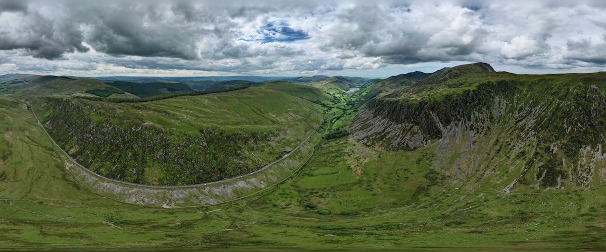 A winding road through a mountainous landscape with green hills and a cloudy sky.