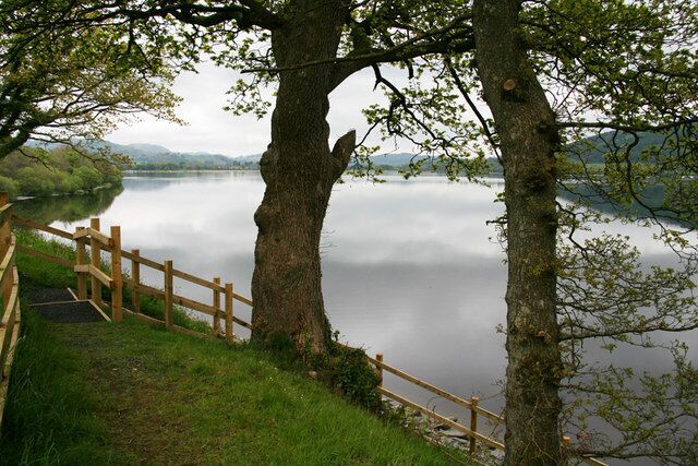 A calm lake with a wooden fence and trees in the foreground.