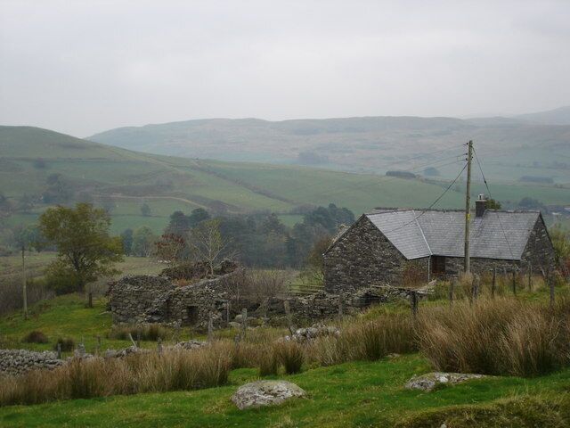 A stone house in a rural landscape with rolling hills in the background.
