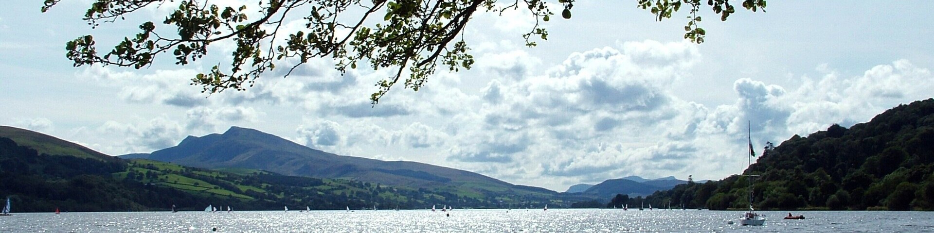 Un lago con barcos, un niño corriendo y colinas al fondo.