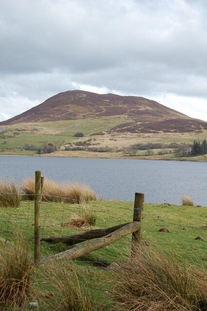 A grassy field with a wooden fence, a body of water, and a hill in the background.