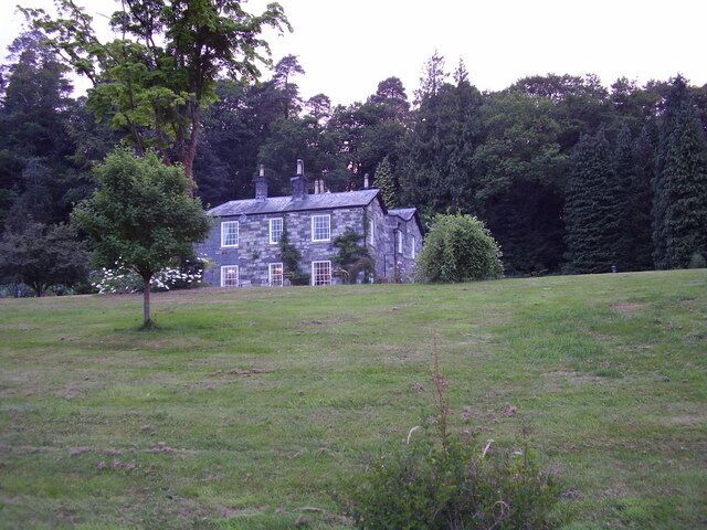 Uma casa de pedra com um gramado bem cuidado e uma grande árvore em primeiro plano.