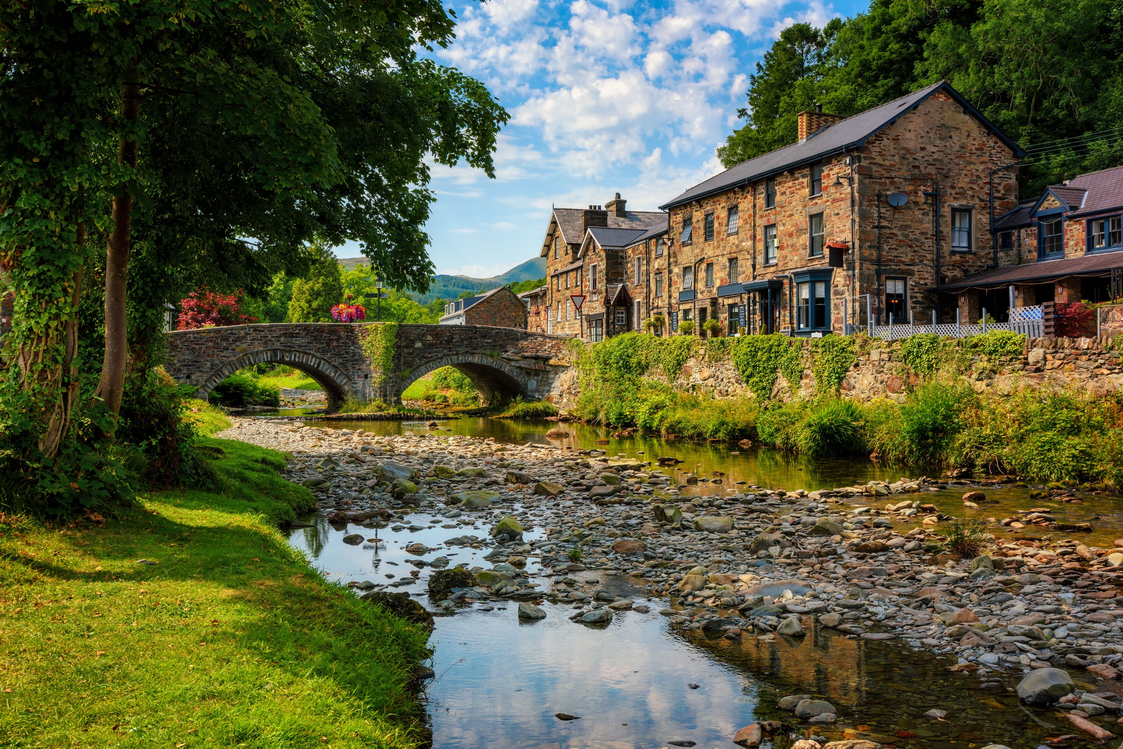 A stone bridge over a river, surrounded by lush greenery and historic stone buildings.