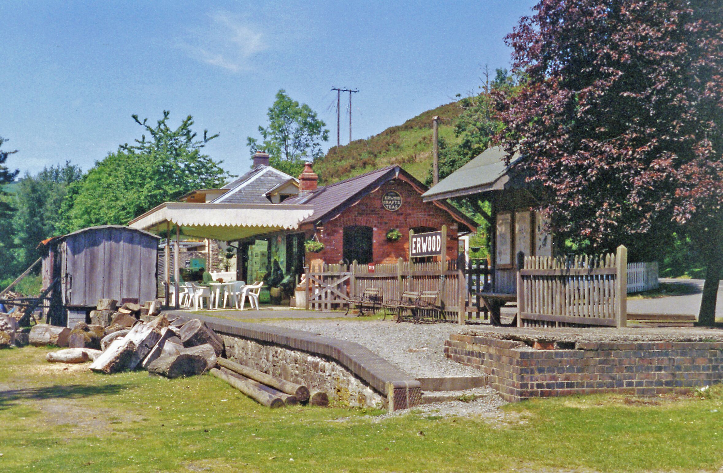 A rustic wooden building labeled "ERWOOD" with a brick facade, surrounded by a wooden fence and a small garden area.