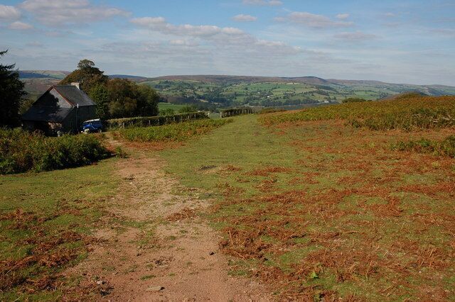 A rural path leading to a house surrounded by fields and hills.