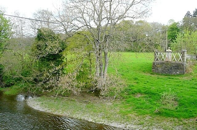 A river with a stone bridge, grassy banks, and leafless trees.