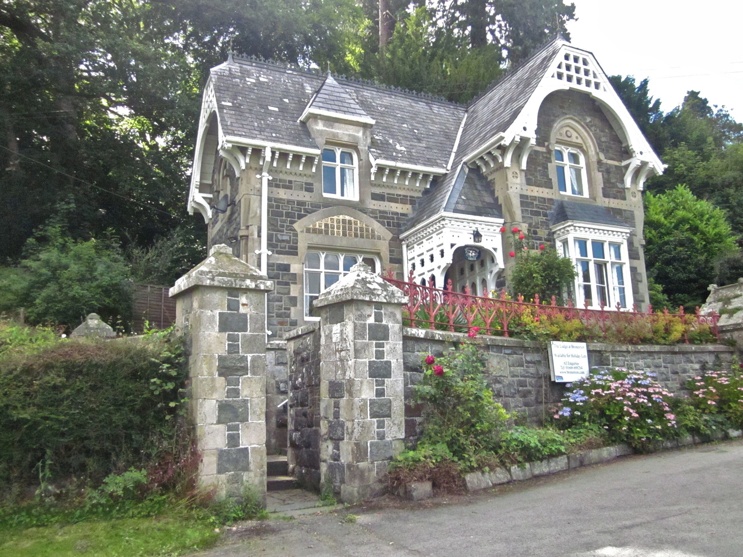 A historic stone building with ornate architecture, a stone gate, and a well-maintained garden with flowers.