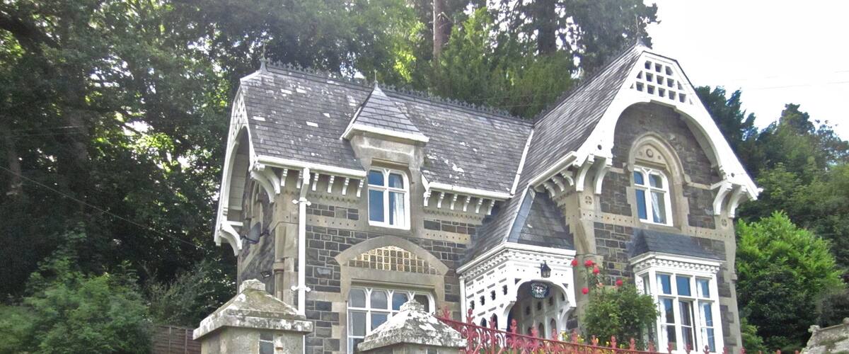 A historic stone building with ornate architecture, a stone gate, and a well-maintained garden with flowers.