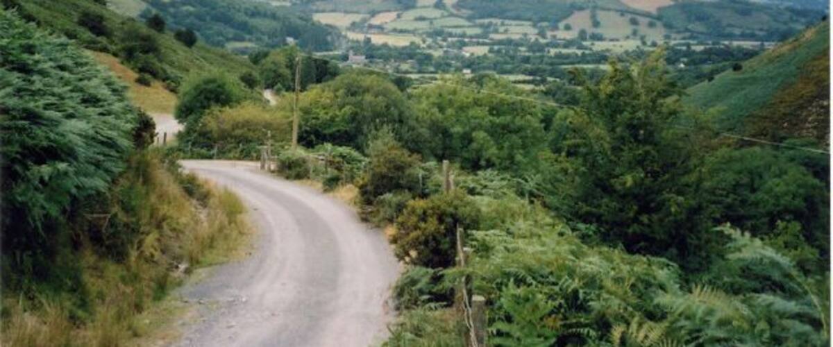 A winding country road through a hilly landscape with lush greenery and distant fields.