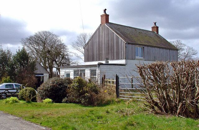 A wooden house with a white exterior, surrounded by a fence and greenery.