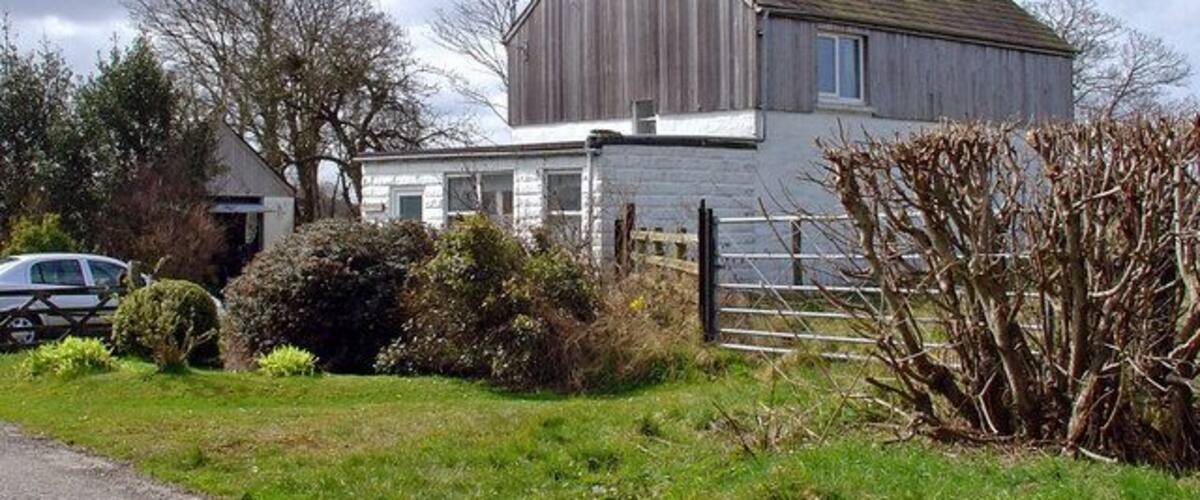 A wooden house with a white exterior, surrounded by a fence and greenery.