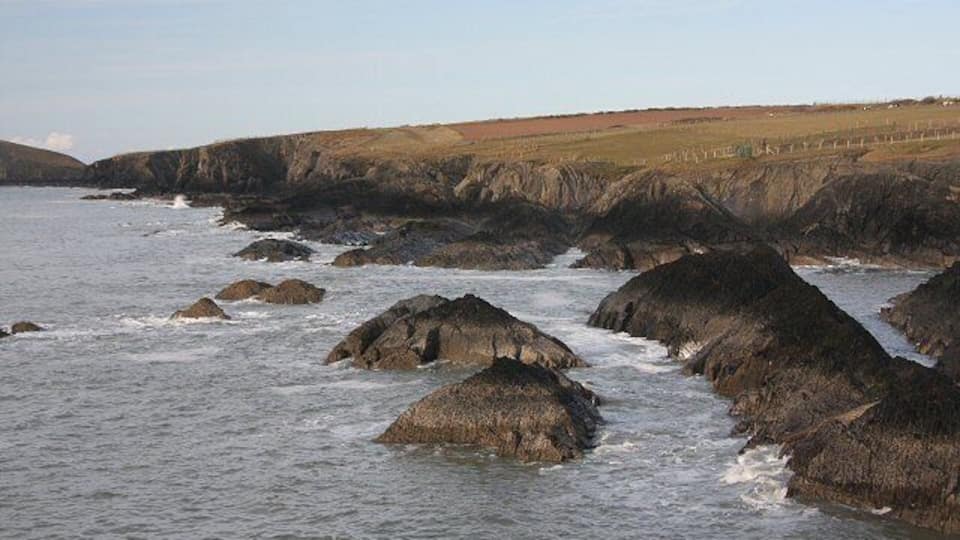 A rocky coastline with waves crashing against large boulders.