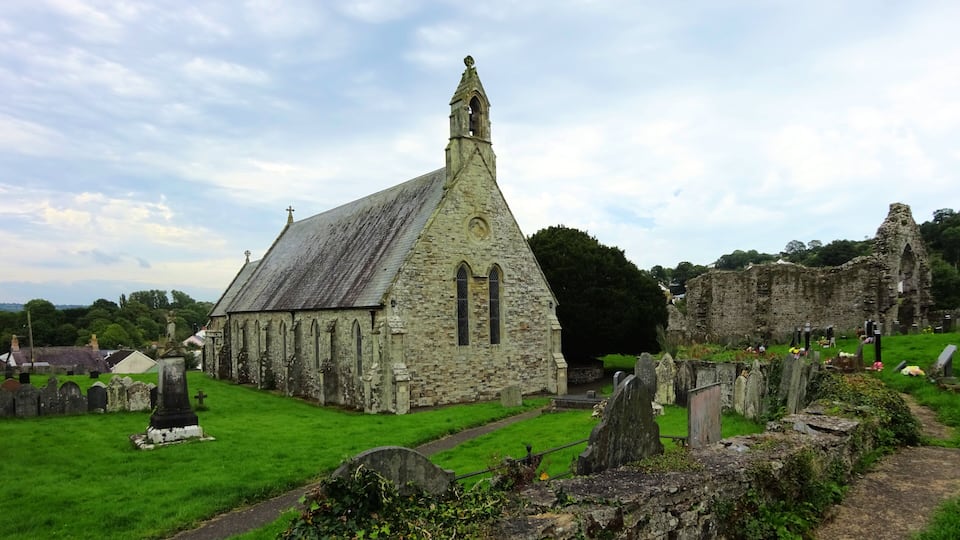 An old stone church with a pointed steeple and a graveyard in the foreground.