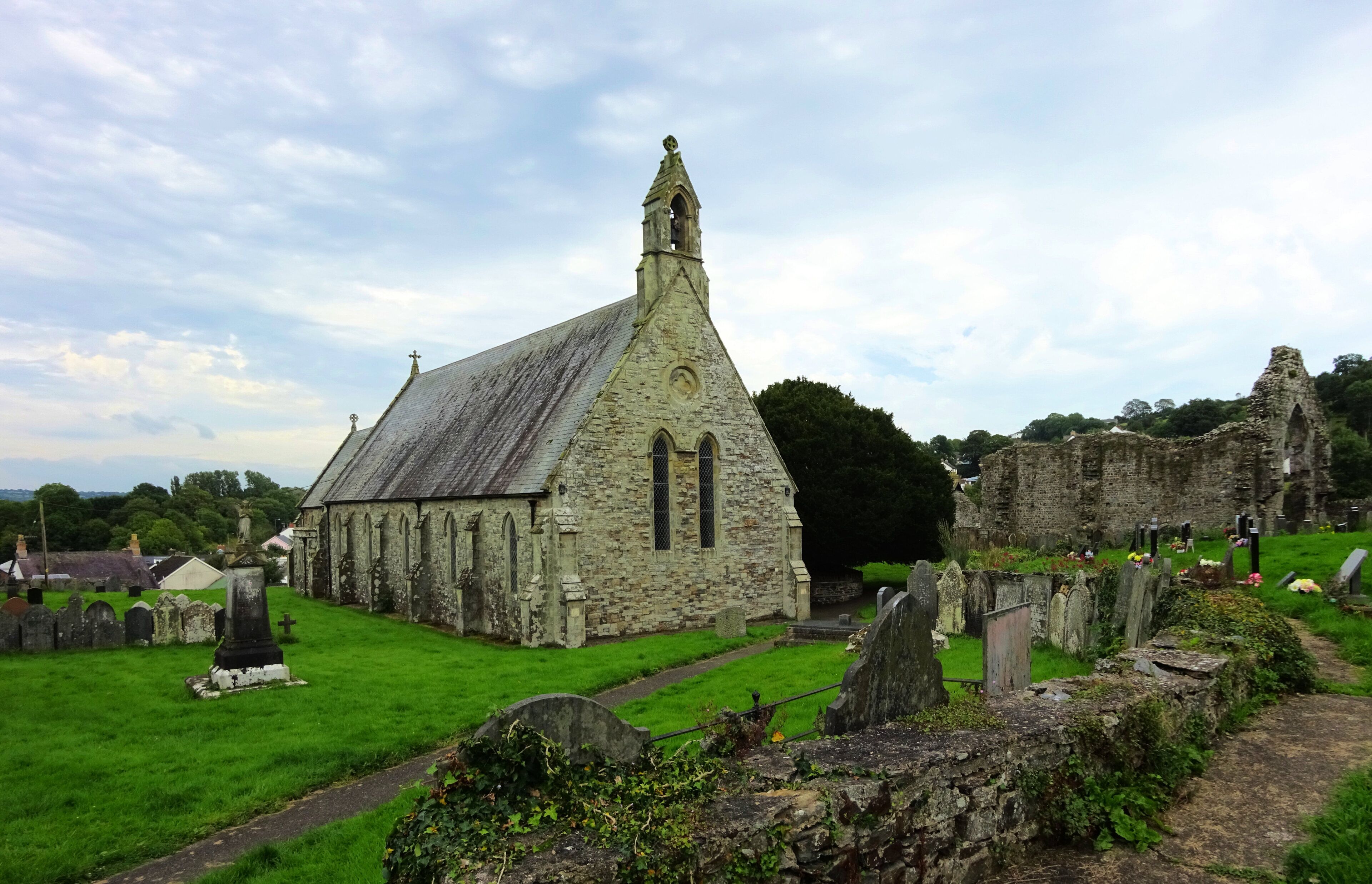 An old stone church with a pointed steeple and a graveyard in the foreground.