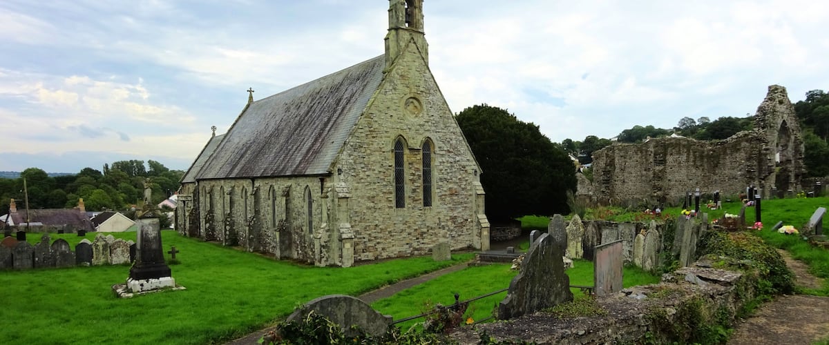 An old stone church with a pointed steeple and a graveyard in the foreground.