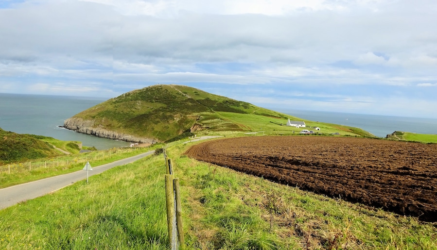 A coastal landscape with a hill, a road, and a white building.