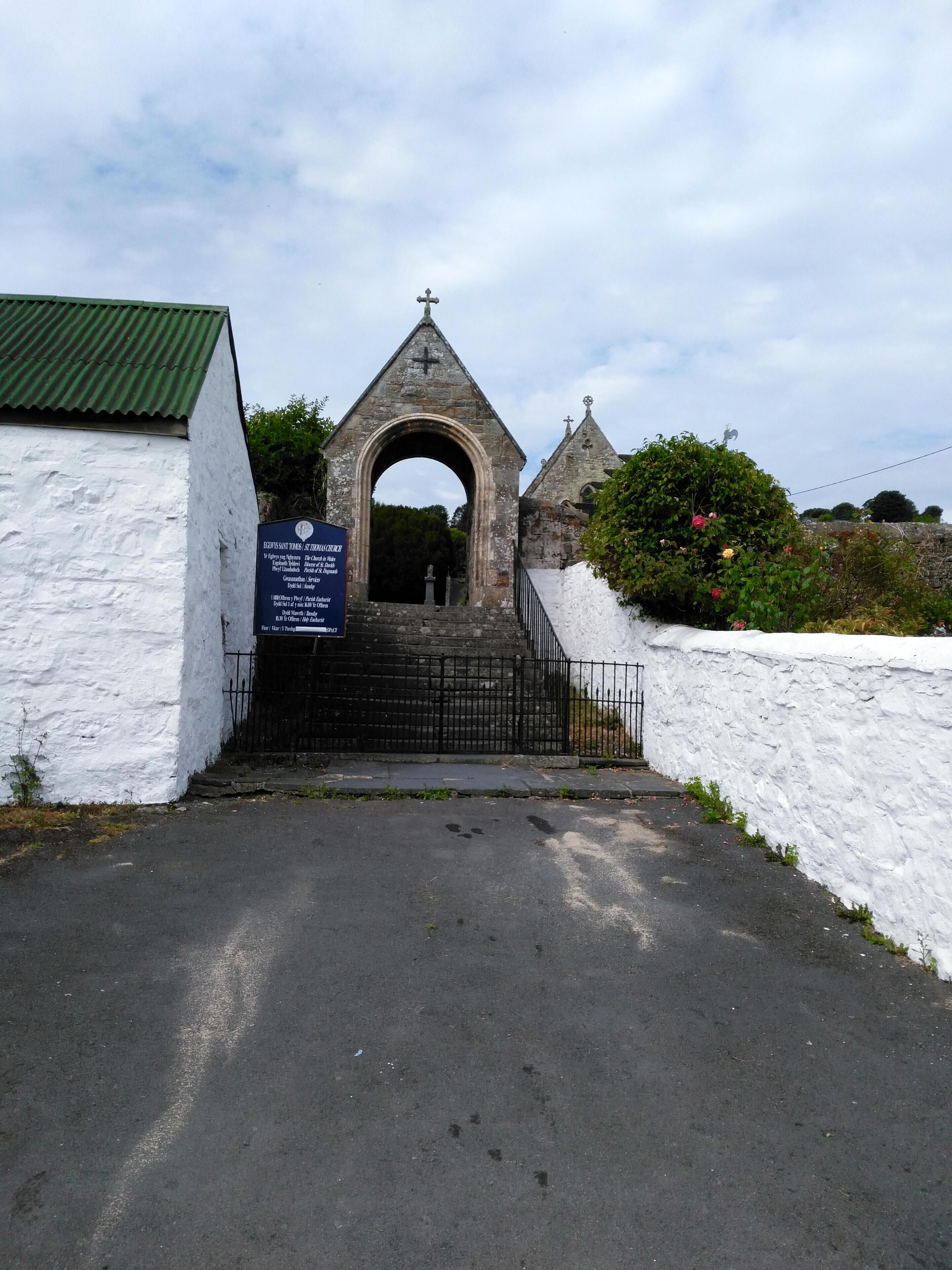 A stone archway leading to a church with a cross on top.