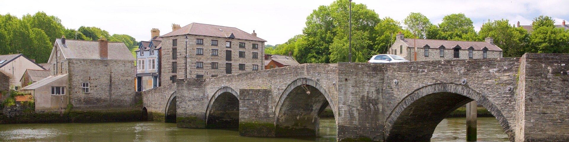 Uma ponte de pedra sobre um rio, com edifícios e árvores ao fundo.