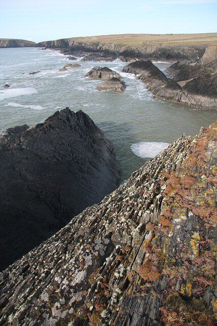 A rocky coastline with waves crashing against large boulders and a rugged sea cliff.