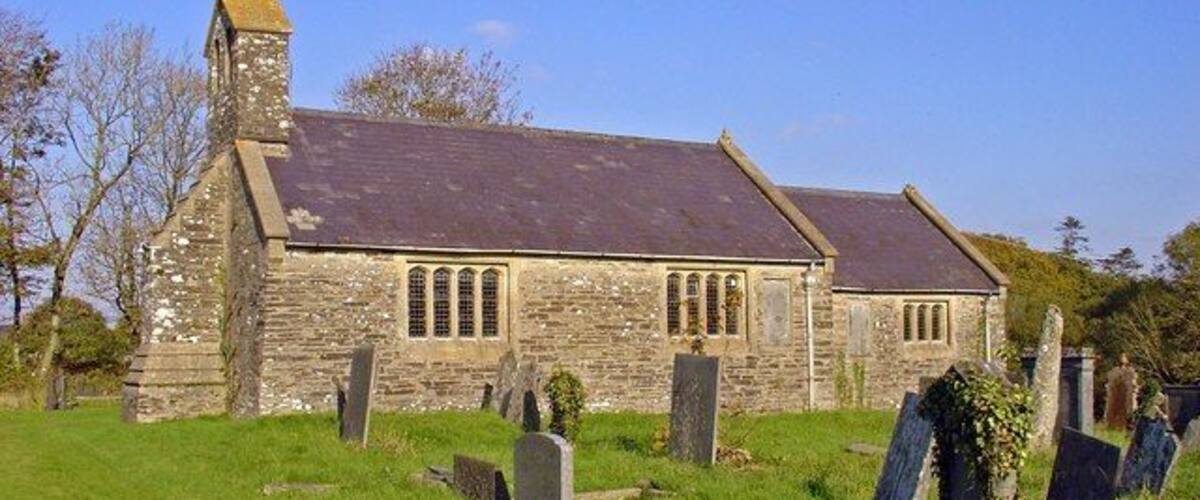 A stone church with a slate roof, surrounded by a cemetery with headstones.