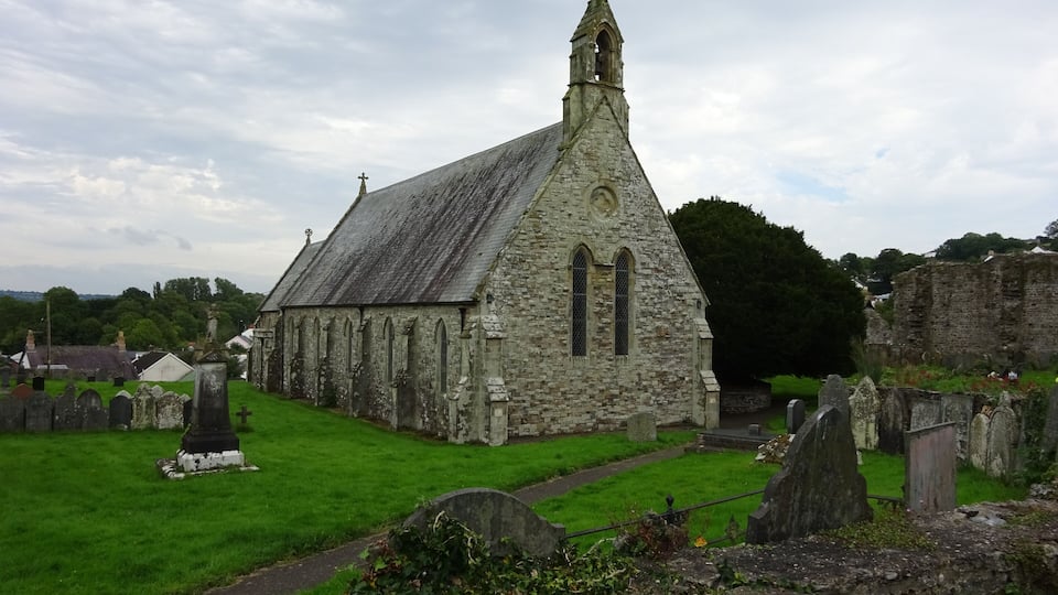 A stone church with a pointed steeple and a graveyard in the foreground.