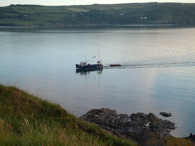 A calm lake with a fishing boat and a wake behind it.