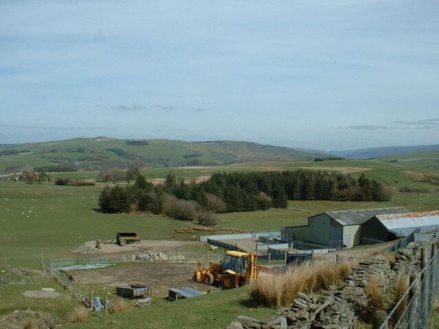 Paisagem rural com uma fazenda, um trator e colinas suaves ao fundo.