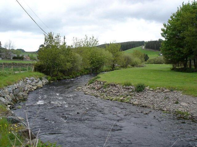 A rocky stream with a stone wall on one side and a grassy field on the other.