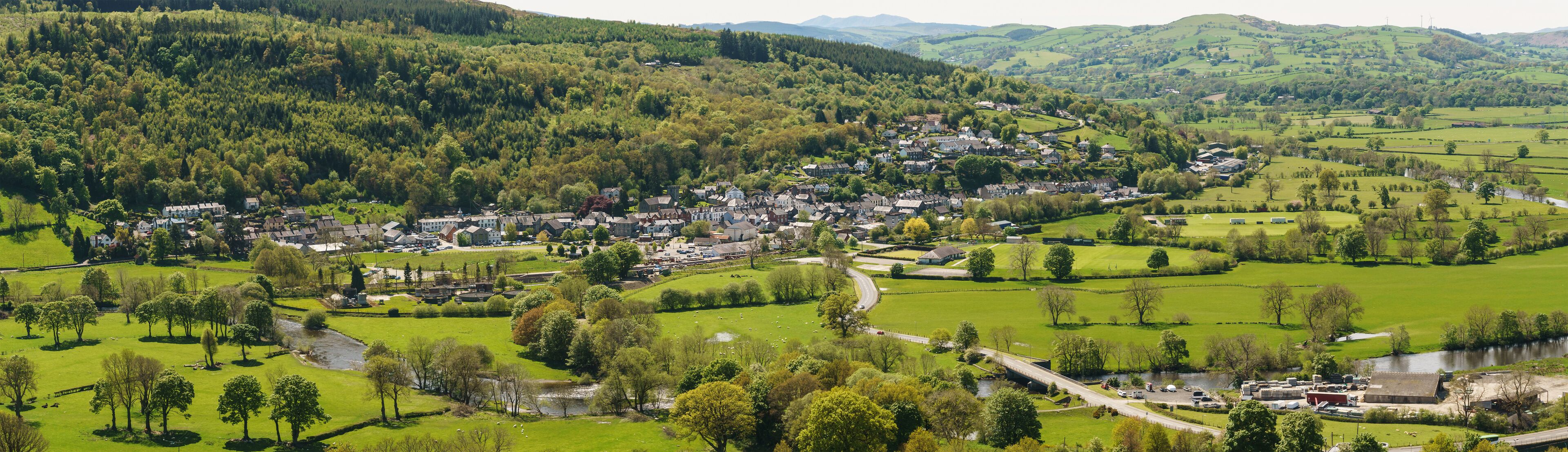 A town nestled in a valley with a river, surrounded by lush green hills and forests.