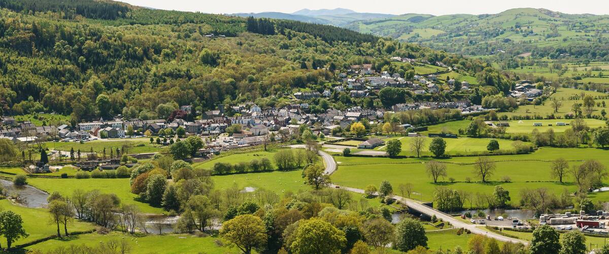A town nestled in a valley with a river, surrounded by lush green hills and forests.